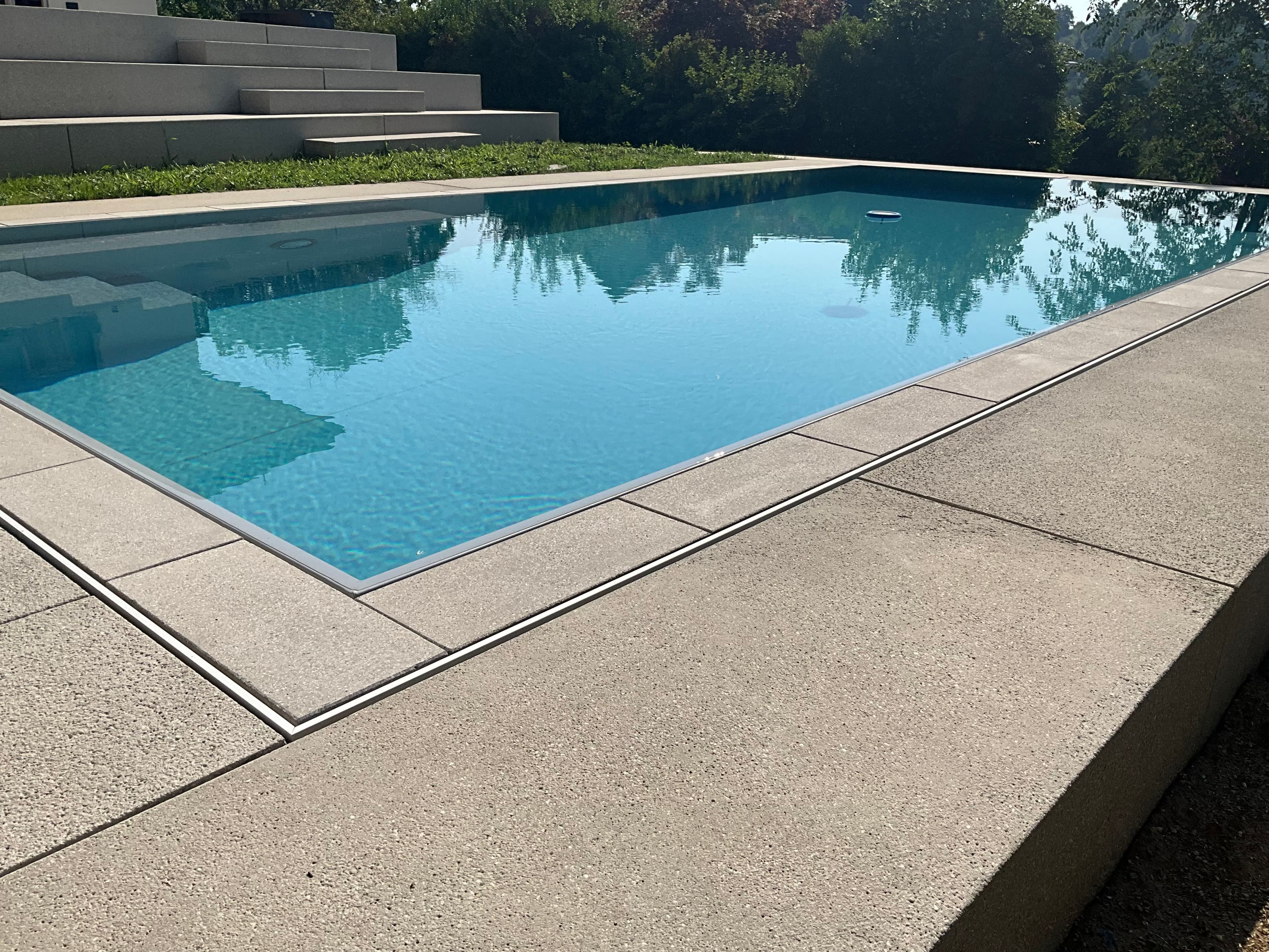 Pool mit Steinbelag, die Überlaufrinne ist im Terrassenbelag integriert