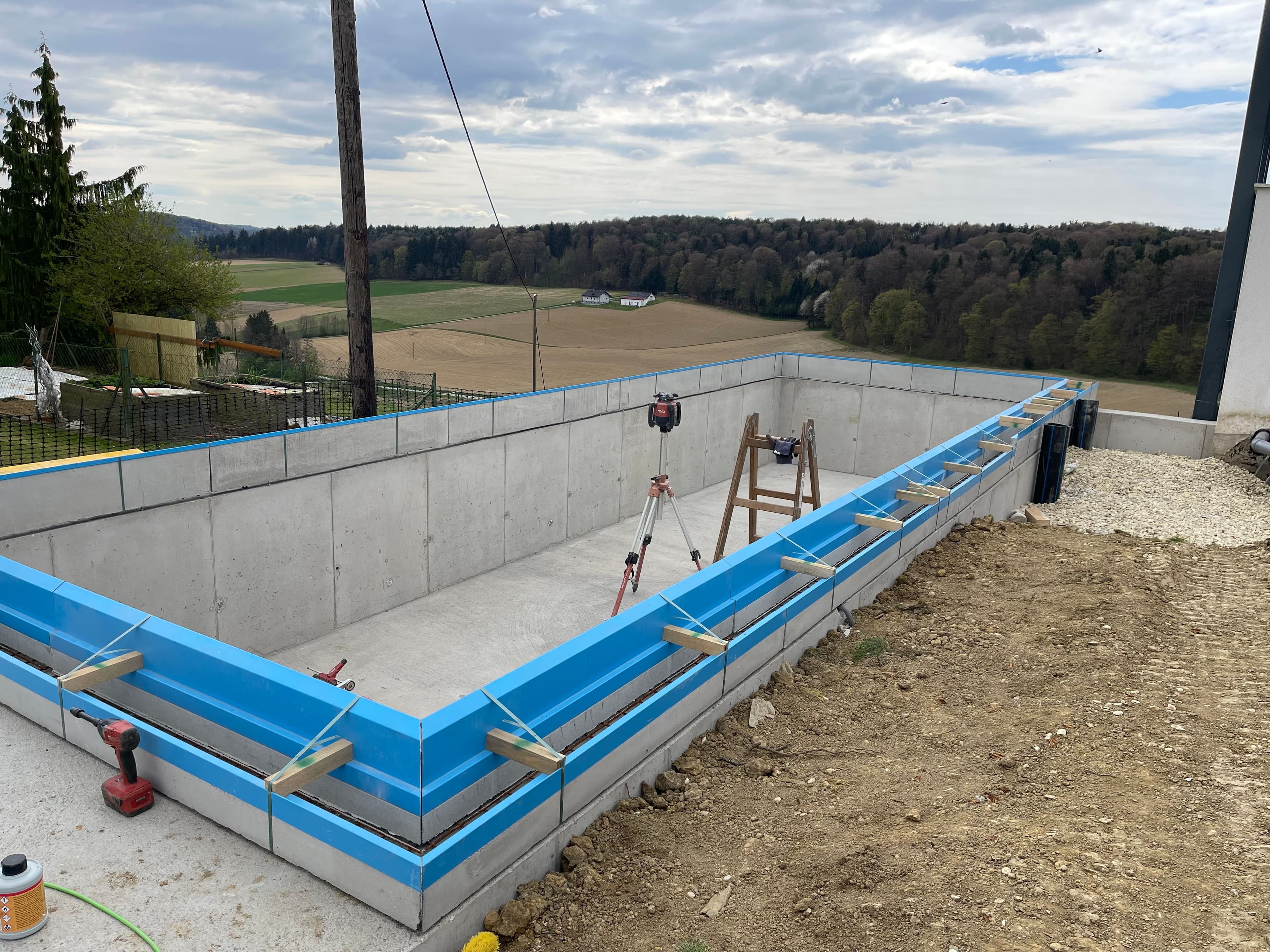 Poolbaustelle: AquaLite-Rinnenelemente auf dem Rohbau-Becken, dahinter die Landschaft